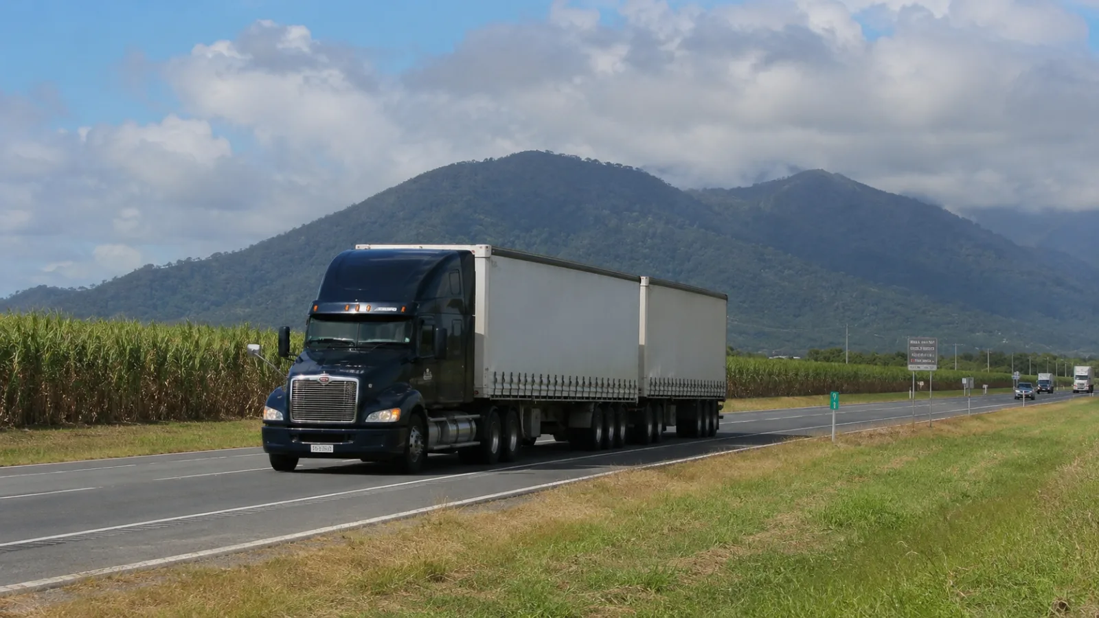 Semi-trailer on the highway between cane paddocks with the ranges behind Mackay