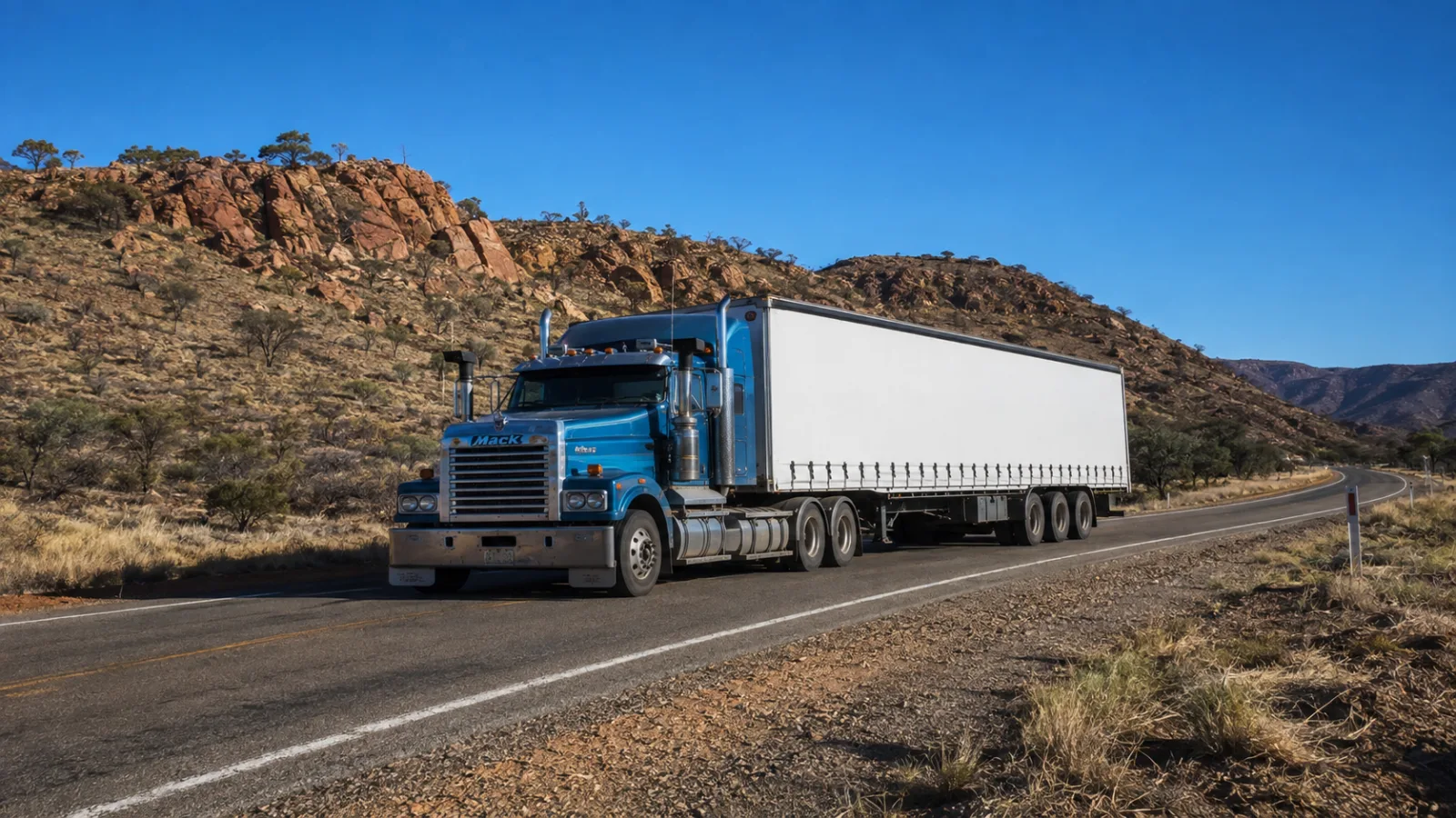 Semi-trailer on the highway between red rocky spinifex ridges near Mount Isa